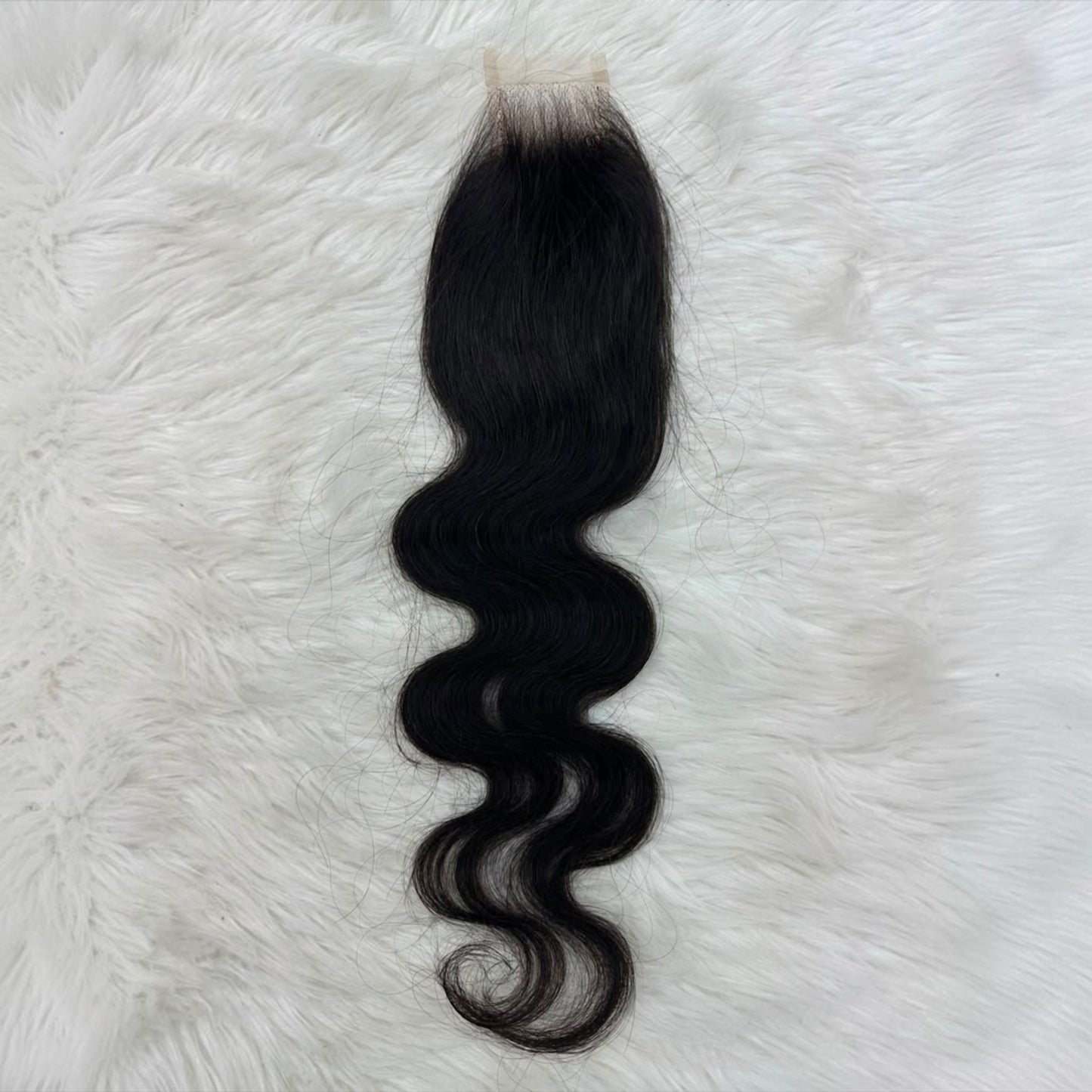 A single 2x6 HD lace closure black body wave with a natural-looking light beige lace base, laid flat on a white faux fur background.