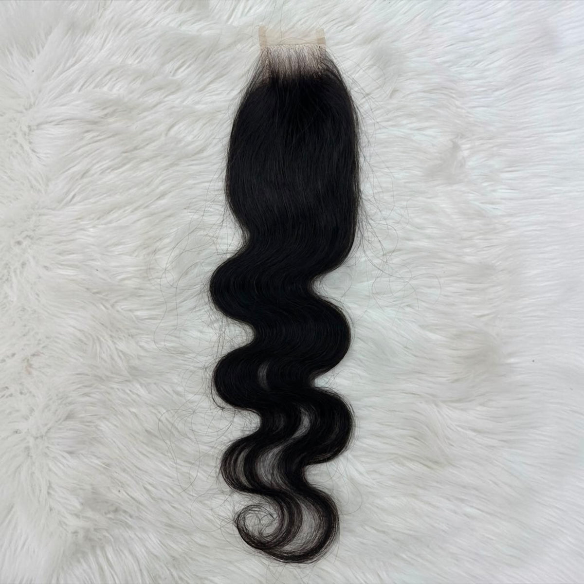 A single 2x6 HD lace closure  black body wave  with a natural-looking light beige lace base, laid flat on a white faux fur background.