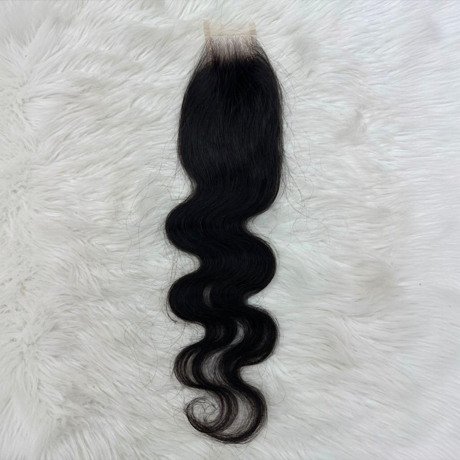 A single 2x6 HD lace closure  black body wave  with a natural-looking light beige lace base, laid flat on a white faux fur background.