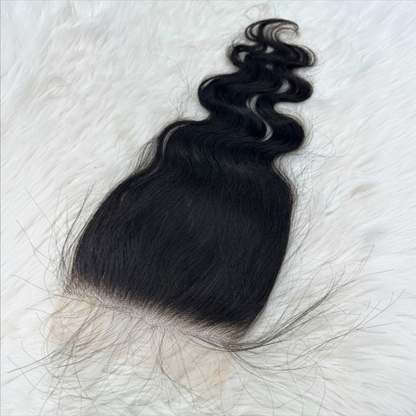 A single 5x5 HD lace closure  black body wave  with a natural-looking light beige lace base, laid flat on a white faux fur background.