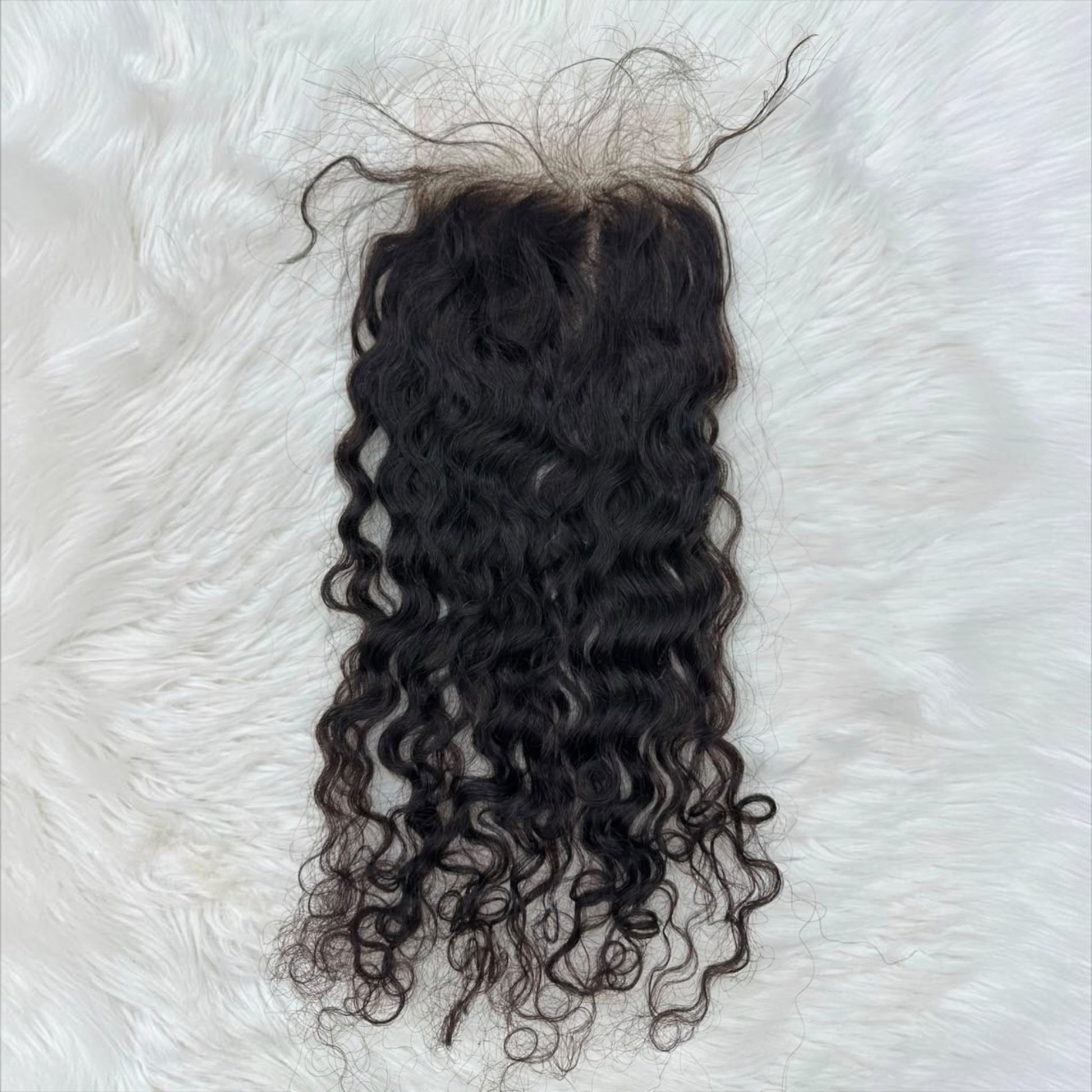 A dark brown to black 5x5 HD lace closure indian curly wave lace frontal wig extension laid flat on a white faux fur background.